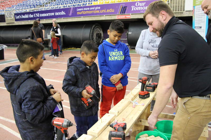 Boys work with volunteer to screw nails into wood boards.